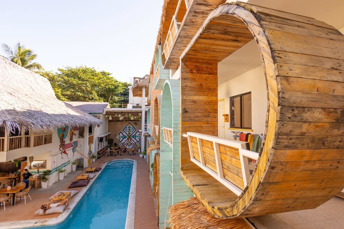 A resort with a pool, wooden structures, and a thatched-roof building.