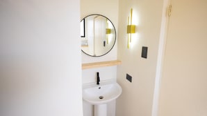 A bathroom with a white sink, a round mirror, and a wall-mounted light fixture.