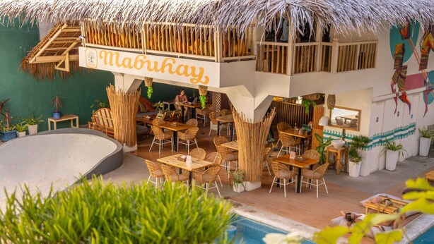 A poolside area with outdoor seating, a thatched-roof structure, and a sign reading 'Mabuhay.'