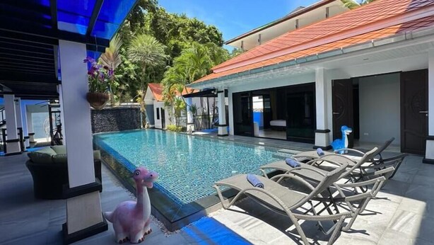 Un espace piscine avec des chaises longues, une petite statue et un coin salon abrité.