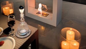Ein gemütlicher Sitzbereich im Freien mit Kamin, Kerzen und einer Glaskaraffe.