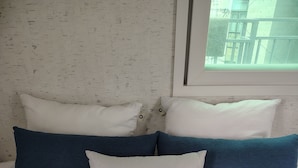 A bed with white bedding and three pillows, one of which is blue.