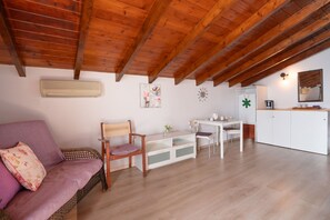 Ein gemütliches Wohnzimmer mit Holzboden, einer Couch, einem Sessel, einem kleinen Tisch und einer Küchenzeile.