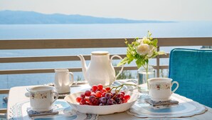 A table set with a teapot, cups, a bowl of grapes, and a vase of flowers on a balcony overlooking a body of water. - Penelope Stone House (Corfu)
