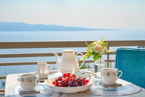 A table set with a teapot, cups, a bowl of grapes, and a vase of flowers on a balcony overlooking a body of water. - Penelope Stone House (Corfu)