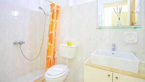Ein Badezimmer mit Dusche, Toilette, Waschbecken und einem Spiegel mit einer Vase.