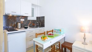Eine kleine Küche mit weißen Schränken, einer Marmor-Spritzschutzleiste, einem kleinen Esstisch mit Stühlen, einer Obstschale und einer Lampe.