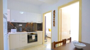 A modern kitchen with white cabinets, a marble backsplash, and a dining area with a wooden table and chairs. - Angela Apartment in Kassiopi (Corfu)