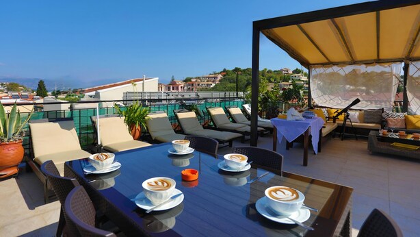 A rooftop terrace with outdoor seating, a table with coffee, and a view of the cityscape. - Angela Apartment in Kassiopi (Corfu)