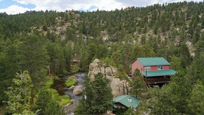 A lodge with a green roof, a river, and a forested mountain backdrop. - Chipmunk Tiny Home at The Woolly Bugger Inn (Estes Park)