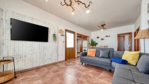 Una sala de estar con un televisor de pantalla plana, un sofá gris con cojines, una mesita de mimbre y un ventilador de techo.