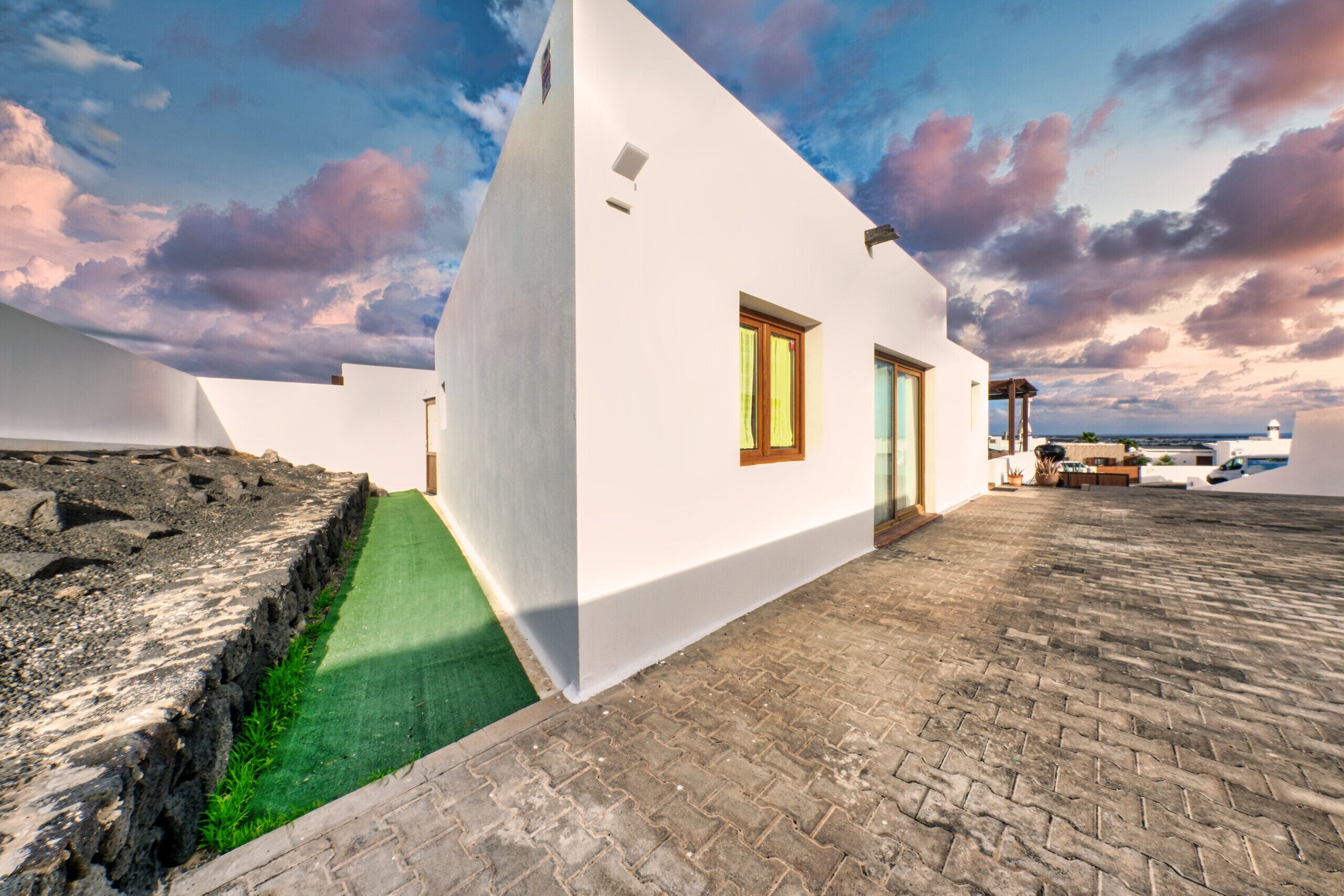 A white building with a paved courtyard and a green artificial turf area.