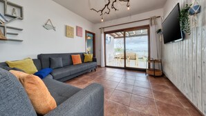 Una sala de estar moderna con un sofá seccional gris, un televisor de pantalla plana montado en una pared de madera y un amplio ventanal corredizo que da a un patio exterior.