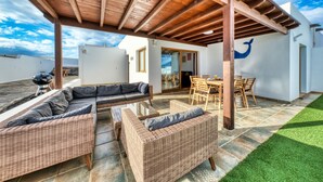 Un patio al aire libre con mobiliario de mimbre, una pérgola de madera y vistas al cielo.