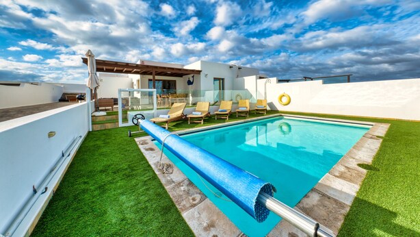 Un área de piscina con cielo azul despejado, un edificio blanco y un césped.