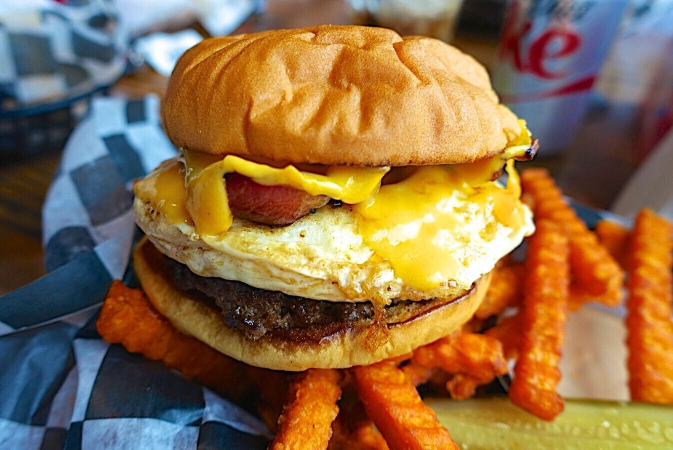A burger with a bun, egg, cheese, and a patty, accompanied by fries and a pickle.