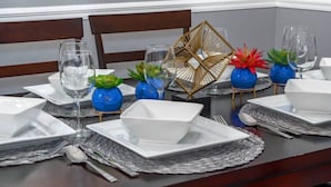 Mesa de comedor dispuesta con platos, tazones y vasos blancos, acompañada de jarrones azules decorativos y un centro de mesa geométrico.