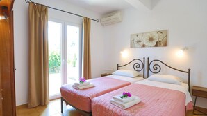 A hotel room with two beds, beige curtains, a large window, and a wall-mounted air conditioner. - Spiros Saint Stephanos (Corfu)