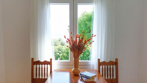 A wooden dining table with a vase of red flowers and a book on it, positioned between two wooden chairs. - Spiros Saint Stephanos (Corfu)
