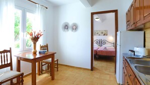 A kitchen with wooden cabinets, a refrigerator, and a dining area with a table and chairs. - Spiros Saint Stephanos (Corfu)