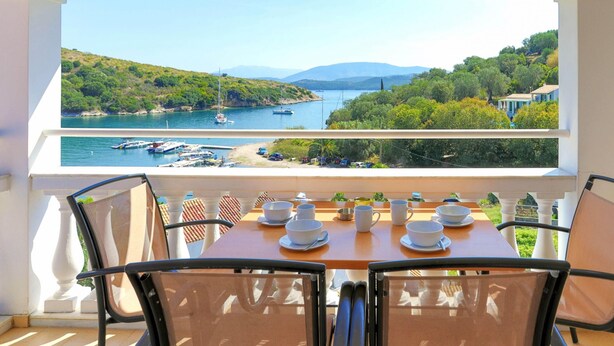 A balcony with a table set for dining, overlooking a marina with boats and a hilly landscape. - Renoula Saint Stephanos (Corfu)