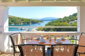 Un balcon avec une table dressée pour le dîner, donnant sur une marina où sont amarrés des bateaux et sur un paysage vallonné.