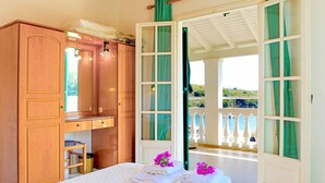 A bedroom with a bed, a wooden wardrobe, and a view of the sea through open doors. - Renoula Saint Stephanos (Corfu)