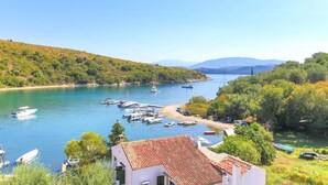 A coastal marina with boats docked, surrounded by lush greenery and hills in the background. - Renoula Saint Stephanos (Corfu)