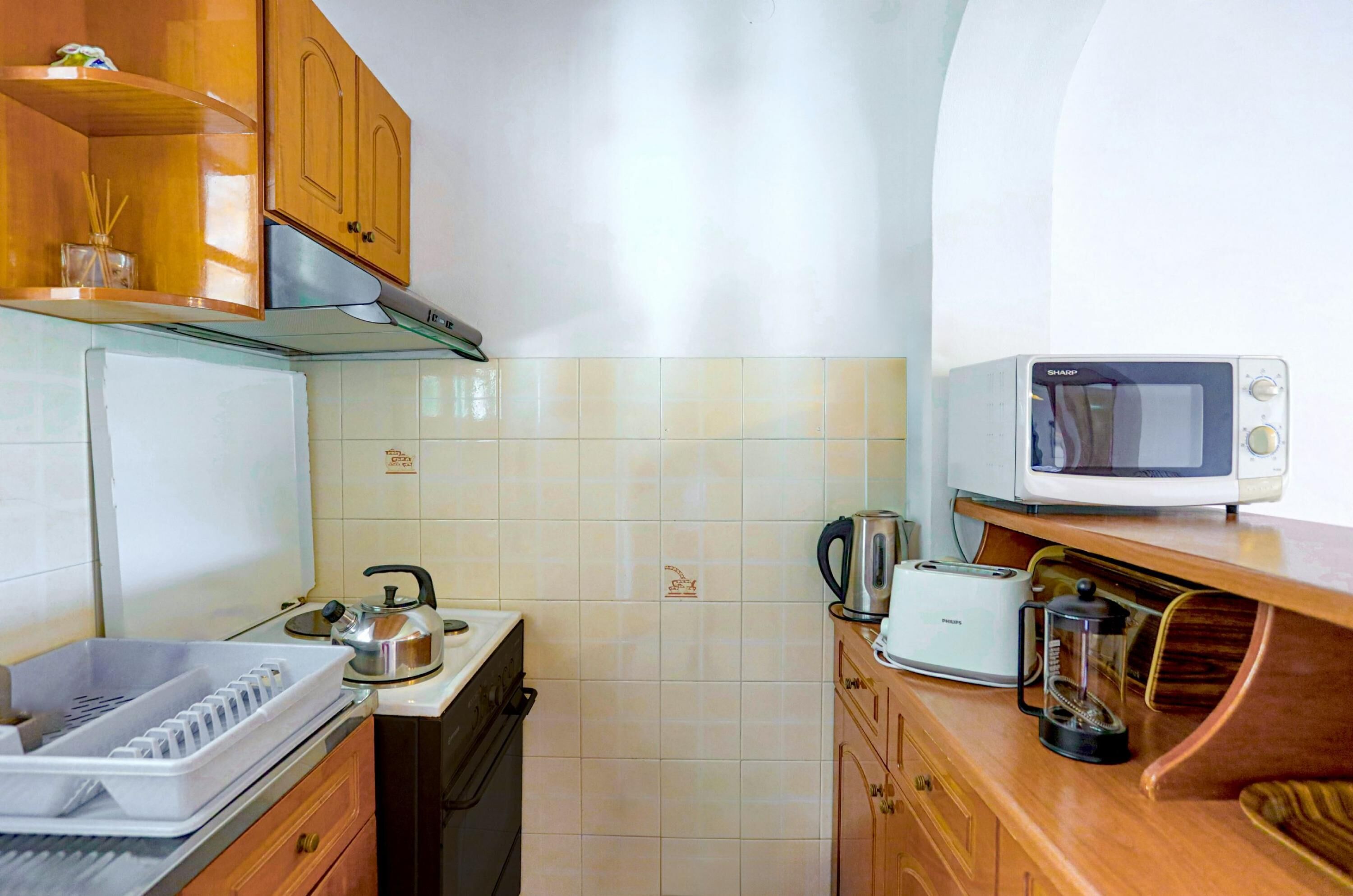A compact kitchen with a microwave, toaster, kettle, and a coffee maker on the counter.