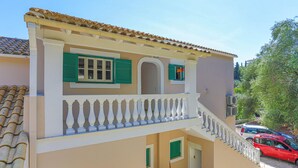 A two-story building with a balcony, a tiled roof, and a red car parked in the driveway. - Renoula Saint Stephanos (Corfu)