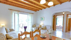 A cozy living room with a wooden ceiling, a dining table set with bowls and cups, and a sofa with striped cushions. - Renoula Saint Stephanos (Corfu)