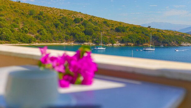 A coastal view with boats, a hill, and a table with a cup and flowers. - Anna Apartment Agios Stephanos (Corfu)
