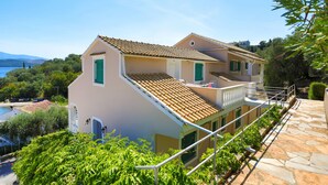 A two-story house with a tiled roof, a balcony, and a stone pathway. - Anna Apartment Agios Stephanos (Corfu)