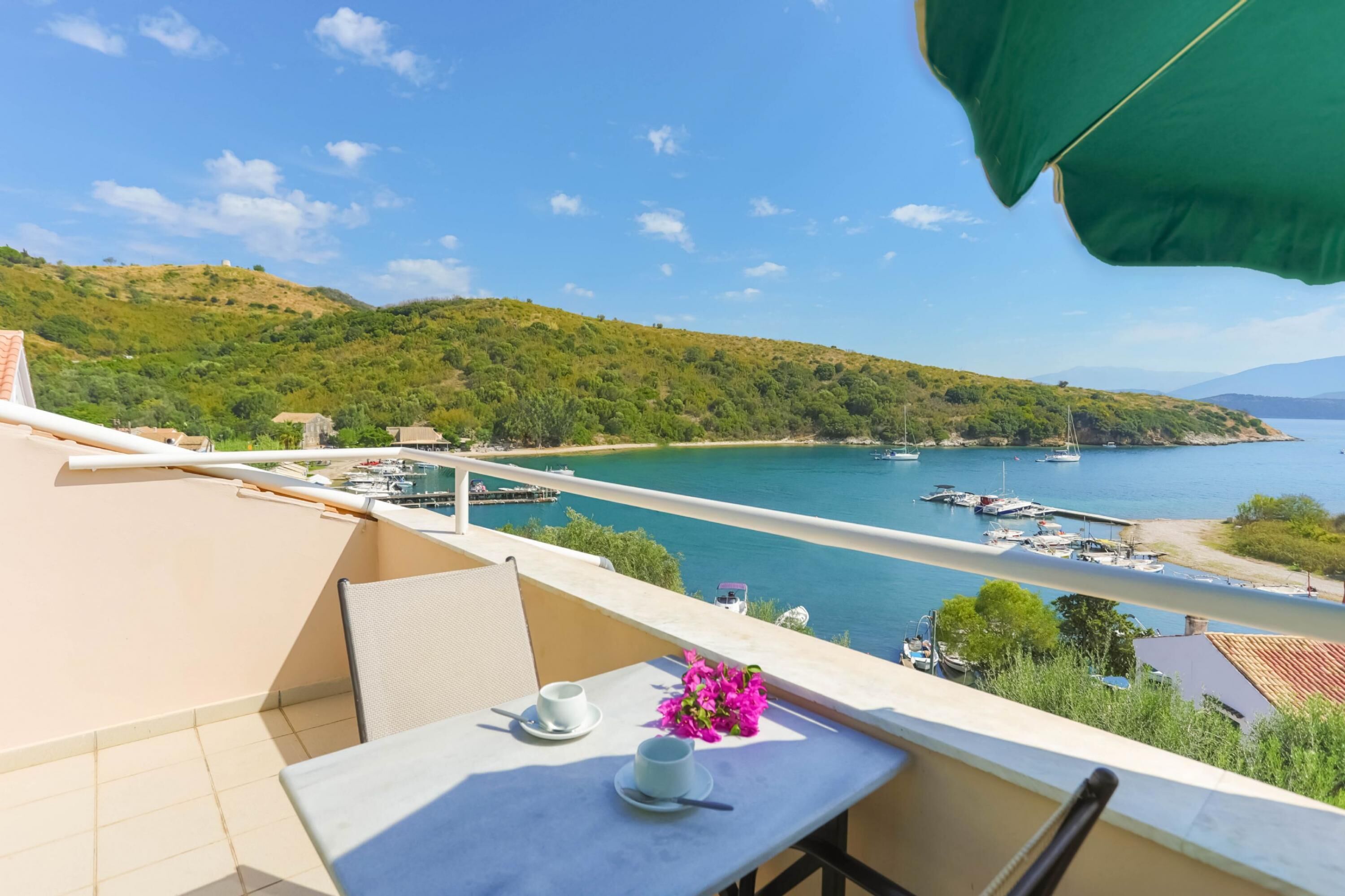 A balcony with a table, chairs, and a view of a coastal area with boats and greenery.