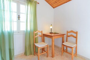 Et lille rum med et træbord og to stole, et vindue med grønne gardiner, samt en lampe på bordet.