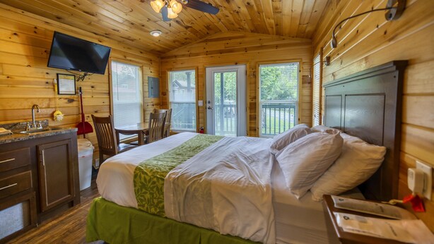 A wooden cabin room with a bed, a desk, a chair, a TV, and a ceiling fan. - Cabin 3 - Everything you need in this Cabin for a great weekend. (Connellsville)