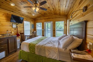Una camera in una casetta di legno con un letto, una scrivania, una sedia, una televisione e una ventola a soffitto.