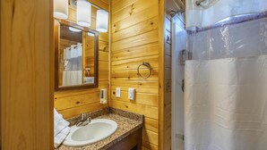 A wooden bathroom with a granite countertop sink, a mirror, and a shower curtain. - Cabin 3 - Everything you need in this Cabin for a great weekend. (Connellsville)