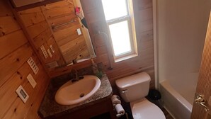 Ein kleines Badezimmer mit Holzwänden, einem Waschbecken, einer Toilette und einer Badewanne.