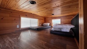 Eine Hütte mit Holzwänden und Holzböden, zwei Betten mit Matratzen, einem Fenster mit Jalousien und einem Dachlüfter.