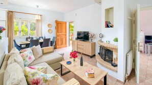A cozy living room with a sofa, dining table, TV, fireplace, and a view of the outdoors. - Villa Divista in Paxi (Paxos)