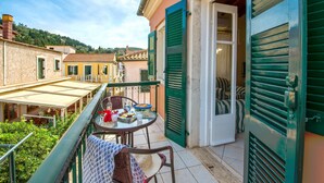 Ein Balkon mit Frühstückstisch, einem Korbstuhl und Blick auf die umliegenden Gebäude und Grünflächen.