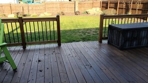 Eine Holzterrasse mit einem grünen Adirondack-Sessel, einer schwarzen Aufbewahrungsbox und einem Holzzaun im Hintergrund.