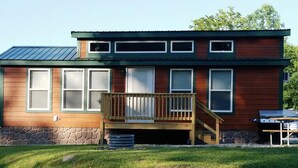 A two-story wooden house with a deck, stone foundation, and a metal roof.