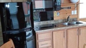 A kitchen with a black refrigerator, wooden cabinets, a granite countertop, a stainless steel sink, and a microwave.