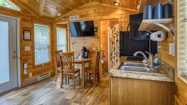 A wooden cabin interior with a dining area, kitchen, and a TV mounted on the wall.