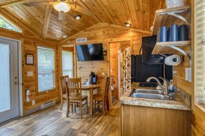L’intérieur d’une cabane en bois comprend un coin repas, une cuisine et un téléviseur fixé au mur.