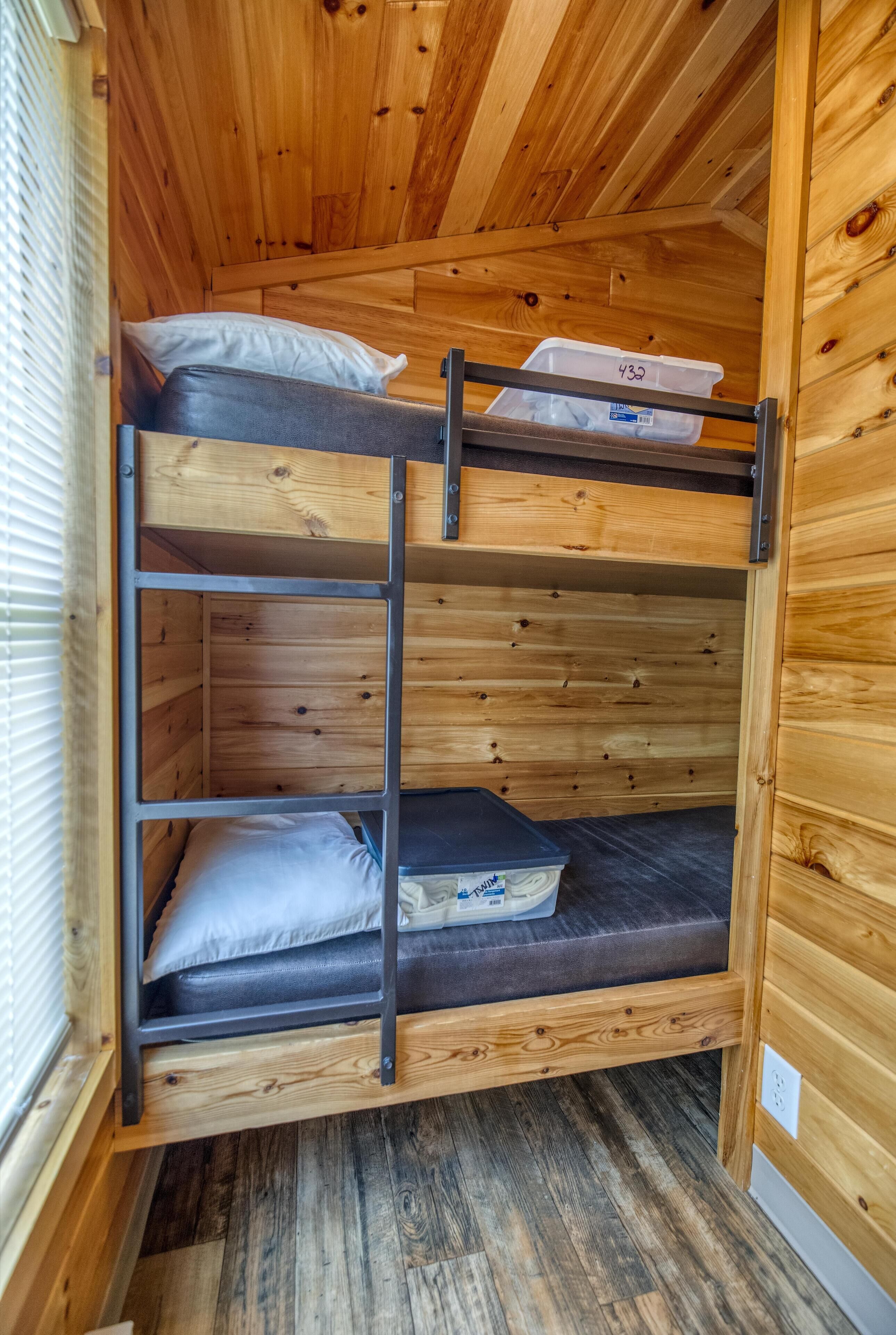 Una cama litera con interior de madera, un baúl de almacenaje etiquetado "433" y una ventana con persianas.