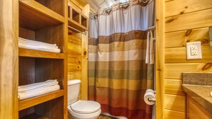 A wooden bathroom with a toilet, shelves with folded towels, and a striped shower curtain.