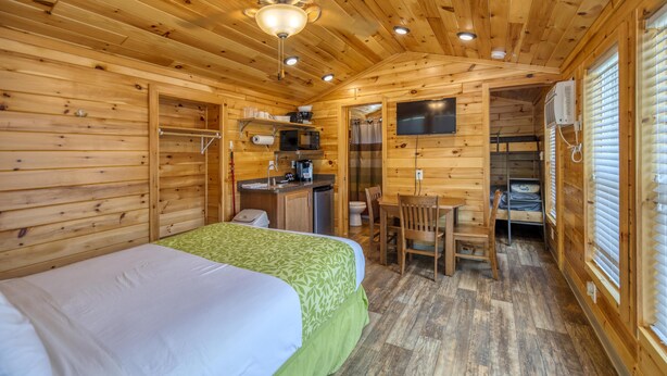 A wooden cabin with a bed, a small kitchenette, a dining area, and a bathroom.